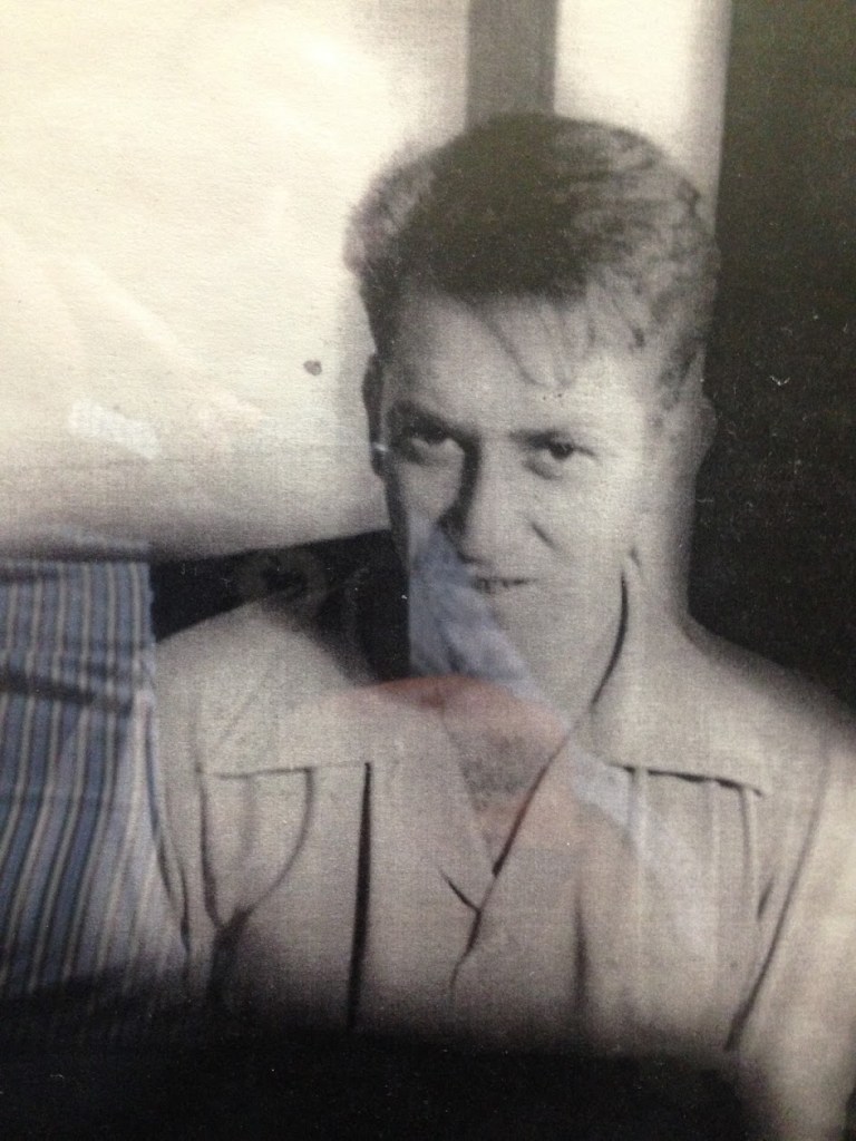 A close-up historical photograph of a young man with short hair, looking at the camera with a serious expression, wearing a collared shirt.